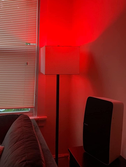 A reviewer's photo of a lamp with a smart bulb installed, casting a vibrant red light.