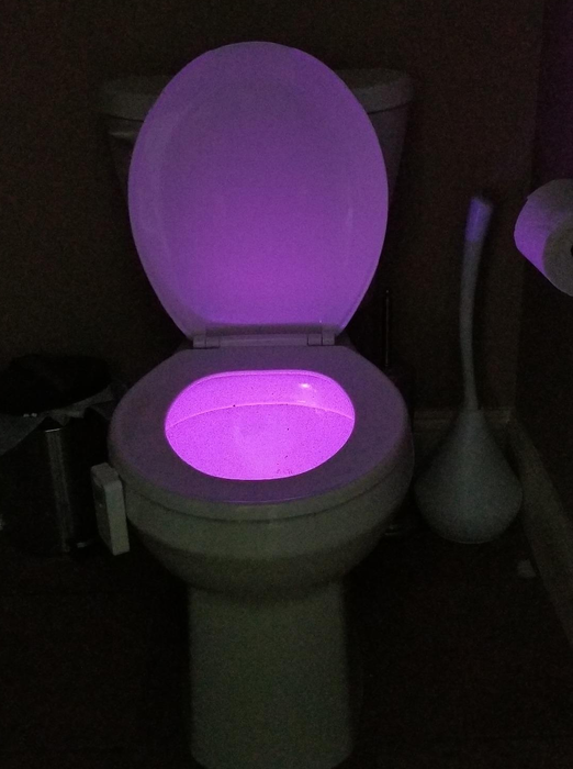 A reviewer's photo showing the light casting a purple glow inside the toilet bowl.