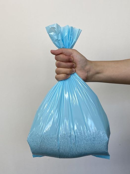 A hand holding a sealed blue plastic bag filled with small white beads, possibly indicating a household item or shopping product