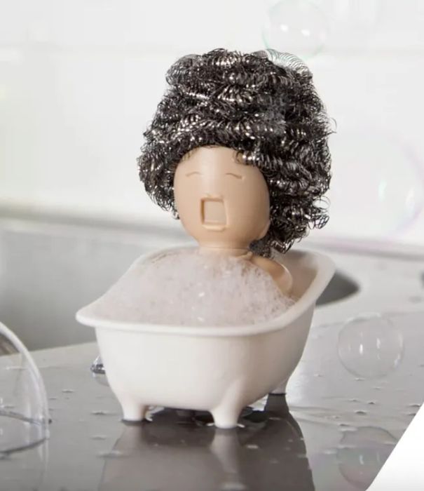 A quirky soap holder shaped like a person lounging in a bathtub, complete with a curly-haired scrubber. A playful touch for any bathroom setting.