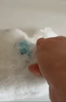 A hand pulling away fluffy sponge to reveal the blue plush