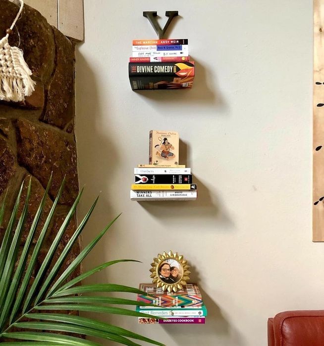 Wall-mounted shelves featuring a selection of books, positioned beside a green potted plant and part of a red chair.