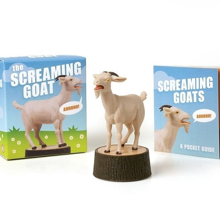 A small plastic goat perched atop a plastic log.