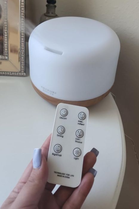 Photo from a reviewer showing a hand holding a remote control in front of an essential oil diffuser placed on a nightstand.