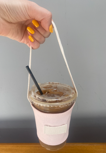An editor holding an iced coffee in a sleeve with a long handle by the hand.