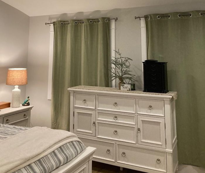 A reviewer photo of a bedroom showcasing a dresser with decorative items and green curtains.