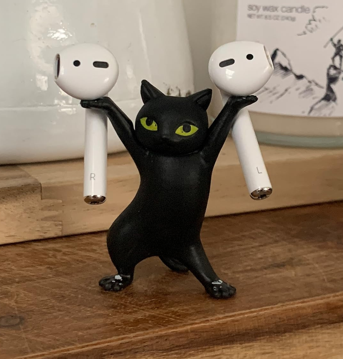 A black cat figurine posed on its hind legs, with an AirPod balanced on each paw.