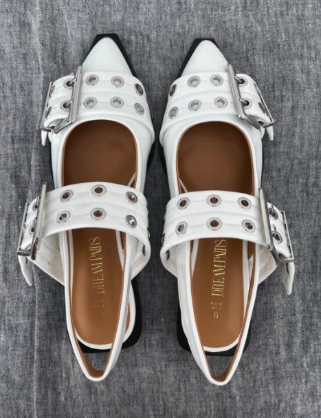 A pair of white slingback flats with pointed toes, embellished with silver grommets and large buckle straps.