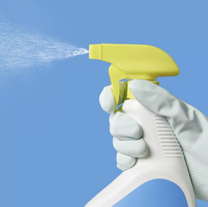 A hand wearing a glove holding a spray bottle, releasing a fine mist
