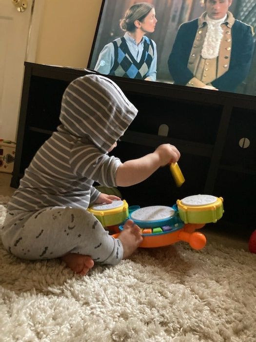 A toddler enjoying playing with a toy drum set.