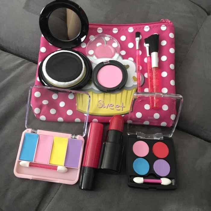 A variety of toy makeup items, neatly arranged alongside a polka-dotted bag on a neutral grey surface.