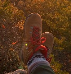 A person relaxing with their hiking boots and patterned socks, feet resting on a rock as they take in the serene nature view.