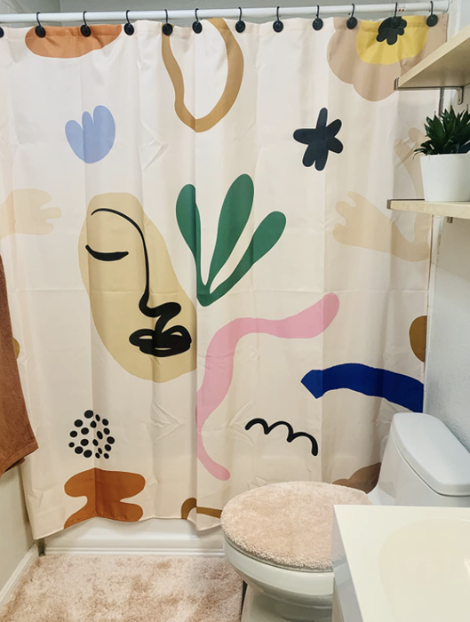 An abstract shower curtain hanging in a reviewer’s bathroom. The design is minimalist, featuring various shapes and a line-drawn face.