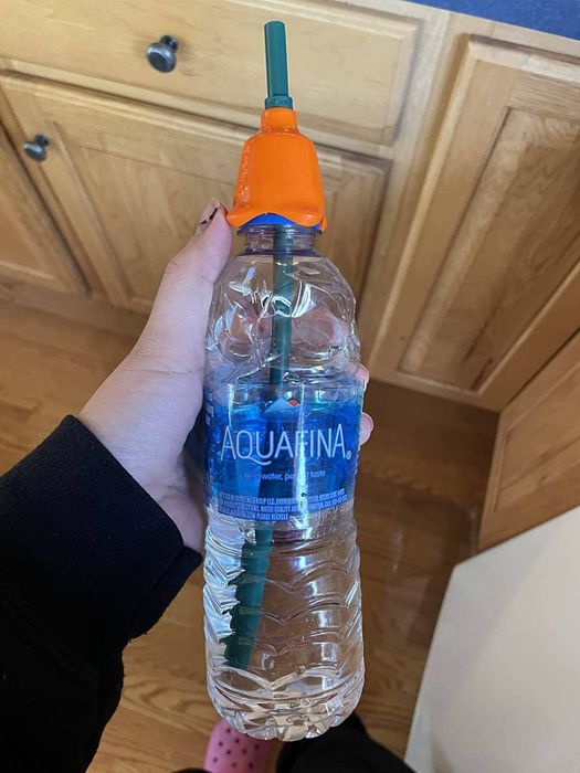 A photo showing a reviewer demonstrating the cap attached to a water bottle with a straw sticking out of it.