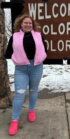 A happy individual poses outdoors, dressed in a pink vest, jeans, and bold pink UGG boots that add a pop of color.
