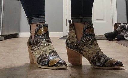 A person wearing ankle-high snake print boots with stacked heels.
