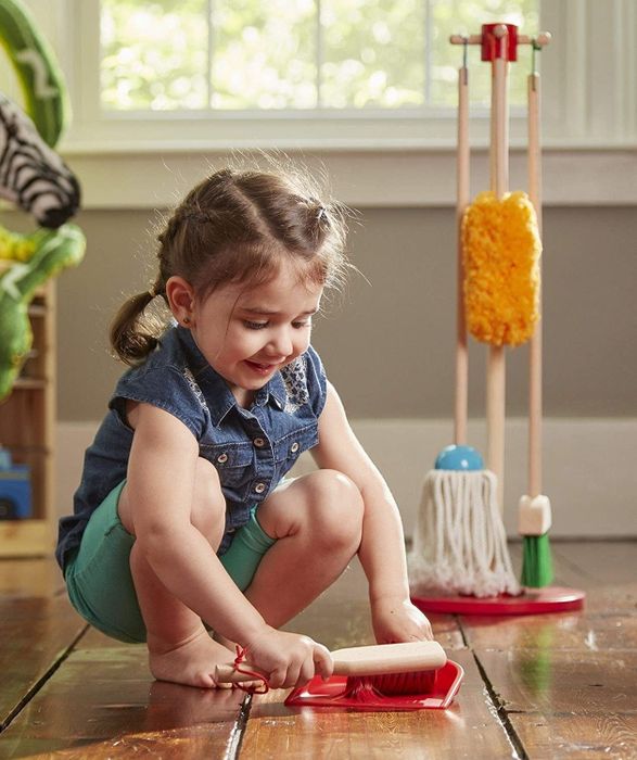 A child happily cleaning the floor with a duster and dustpan, getting involved in tidying up.