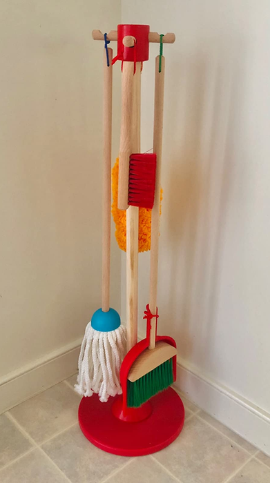 A broom, mop, duster, brush, and dustpan neatly arranged on a wooden organizing stand, ready for cleaning duties.