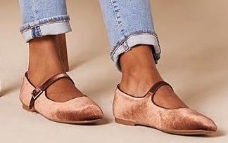 Close-up of a person wearing rolled-up jeans and rose gold velvet Mary Jane flats