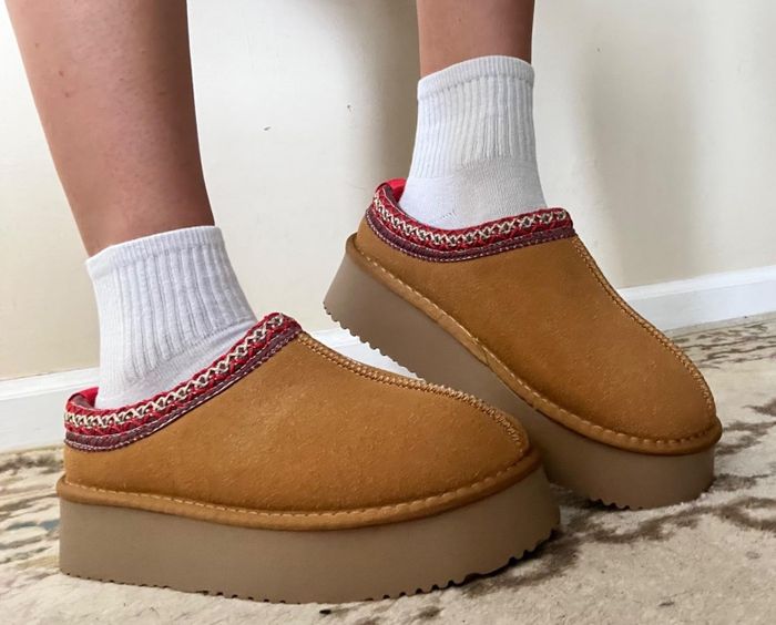 A close-up shot of a reviewer's feet wearing white socks and camel-colored platform slip-on shoes with red trim detailing.