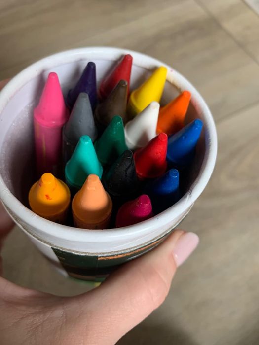An overhead view of a hand holding a cup filled with a variety of crayons, perfect for sparking creativity in your little one.