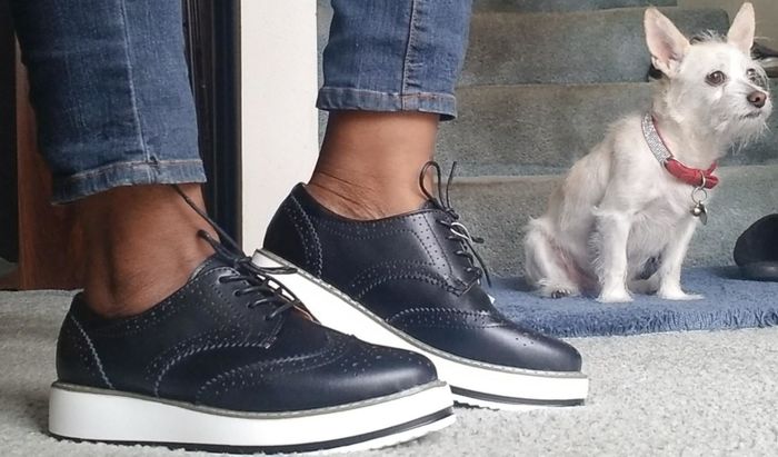 A reviewer's photo featuring someone in jeans, navy platform oxfords, with a dog playfully posing in the background.