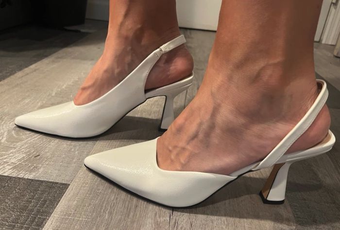 A close-up shot of a person's feet, featuring chic white slingback high heels with pointed toes.