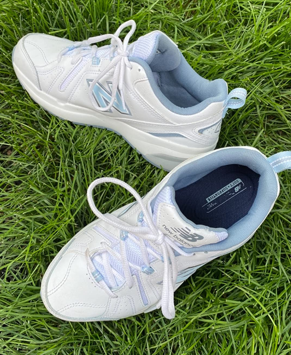 A reviewer shows off the white and blue sneakers against a patch of grass