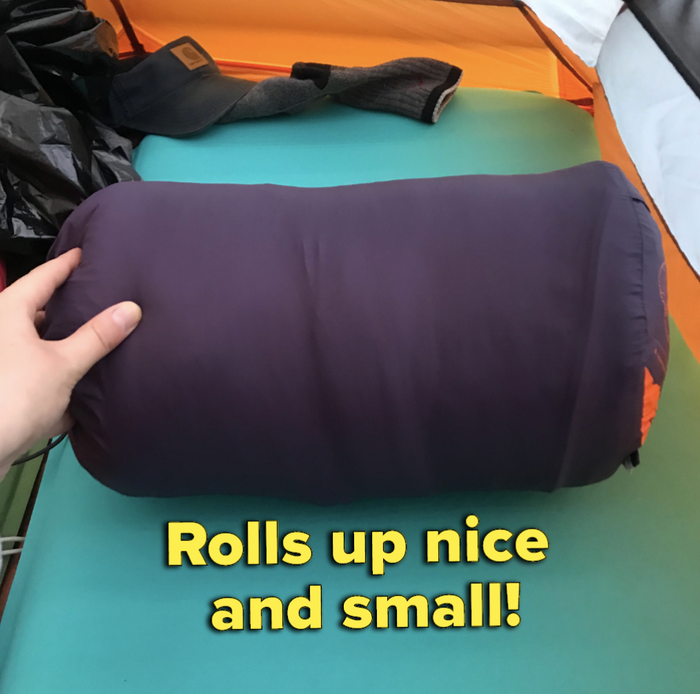 The bag tucked into a compact purple stuff sack labeled 'rolls up nice and small'