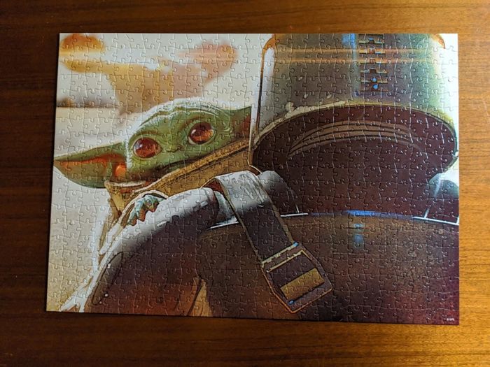 A completed Baby Yoda puzzle with the little character peeking over the Mandalorian's shoulder.