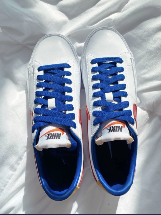 A pair of white Nikes featuring blue laces, blue heels, and a red swoosh.