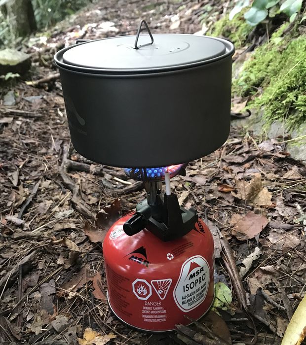 The writer's pot and lid resting atop a small, glowing camp stove, ready for use during a night under the stars.