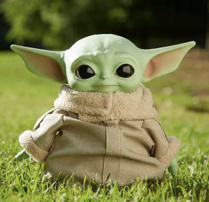 The Baby Yoda plushie dressed in a cute tan coat outfit.