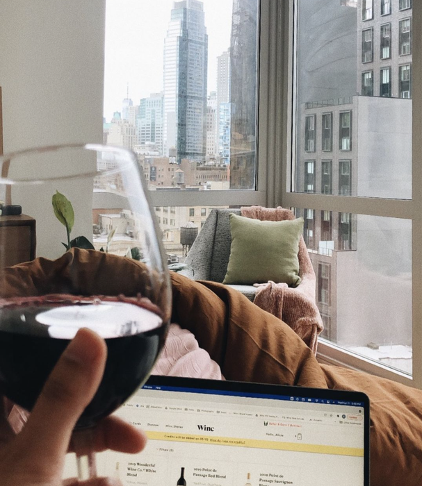 A person holding a glass of red wine while browsing Winc's website.