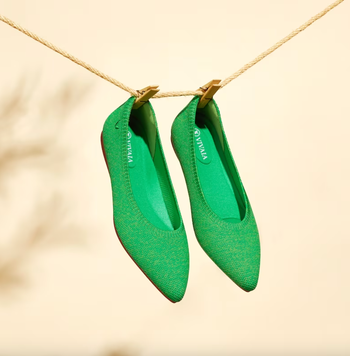 A pair of green pointed-toe flats hanging delicately on a clothesline.