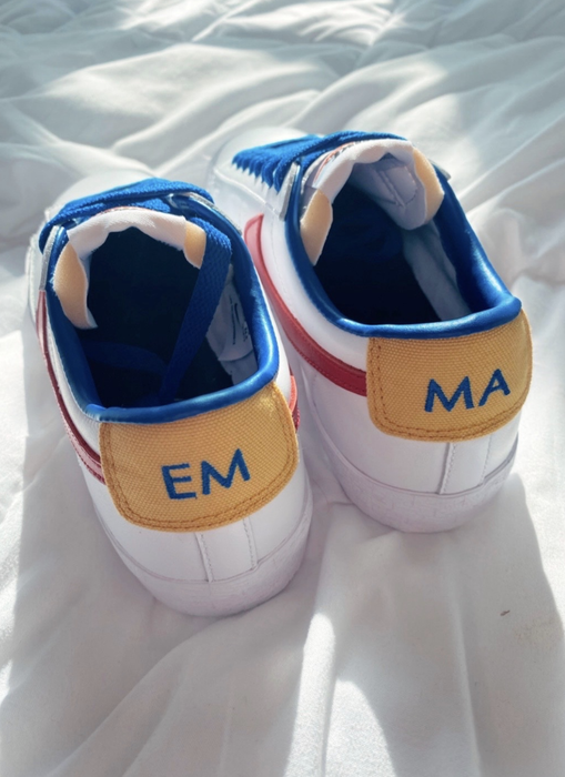 The same white Nikes from the back, showcasing yellow on the heels, with one shoe reading