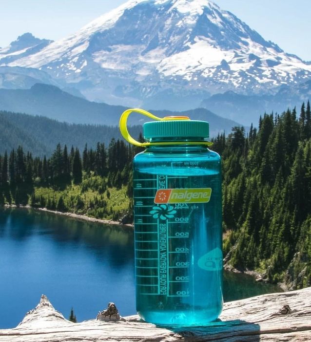 A teal Nalgene in front of a lake and mountains