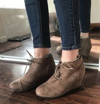 A reviewer wearing brown suede wedge boots
