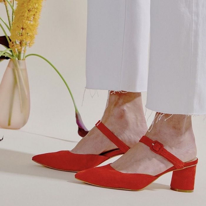 A model dressed in white pants, paired with red suede mules.