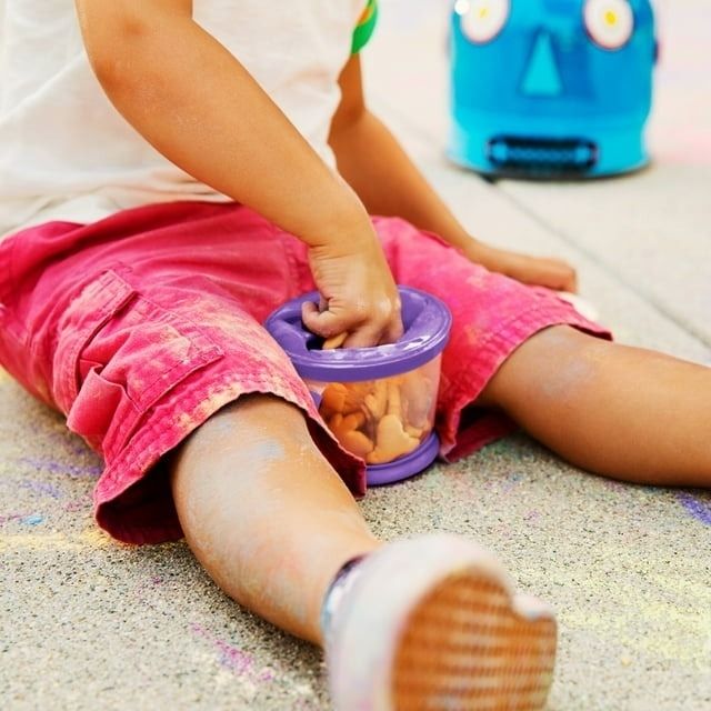A baby hand reaching into a purple snack cup.