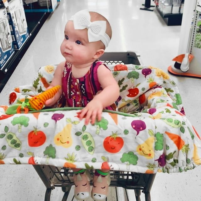 A baby seated in a shopping cart, protected by the cover.