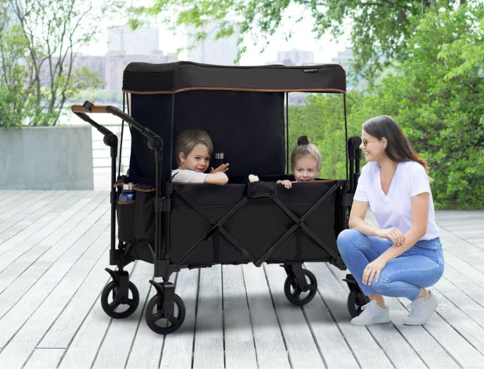 A woman kneeling in front of the wagon, which holds two children inside.