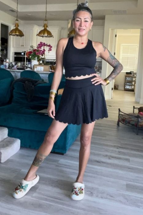 A reviewer wearing a scalloped black crop top and skirt set, paired with Crocs.