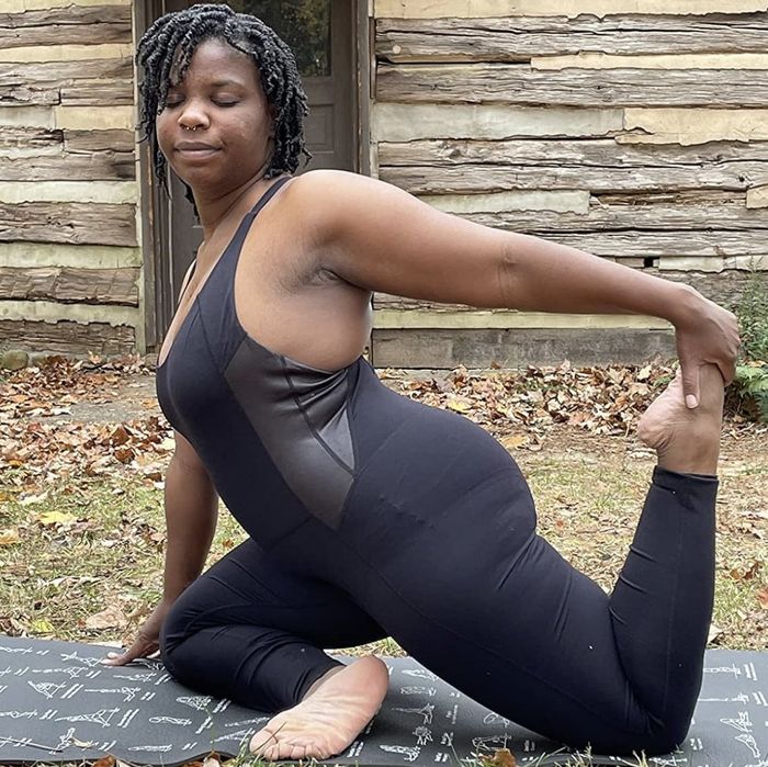 A person in a yoga pose on a mat in front of a rustic wooden building.