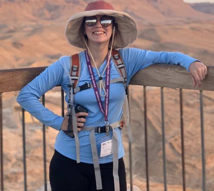 A woman in a sun hat and sunglasses leaning on a railing outdoors, with a lanyard around her neck.