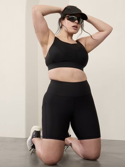 A person in athletic wear, sporting a cap and sunglasses, striking a pose with their hands behind their head.