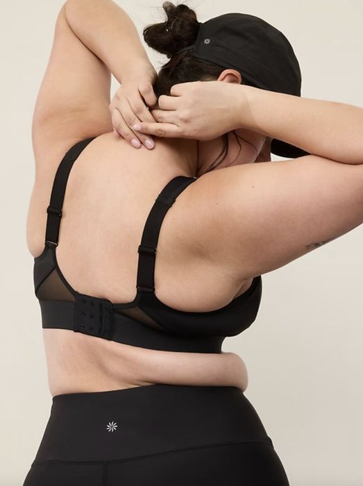 A model adjusting the straps of a black back-fastening bra, with their face not visible in the shot.
