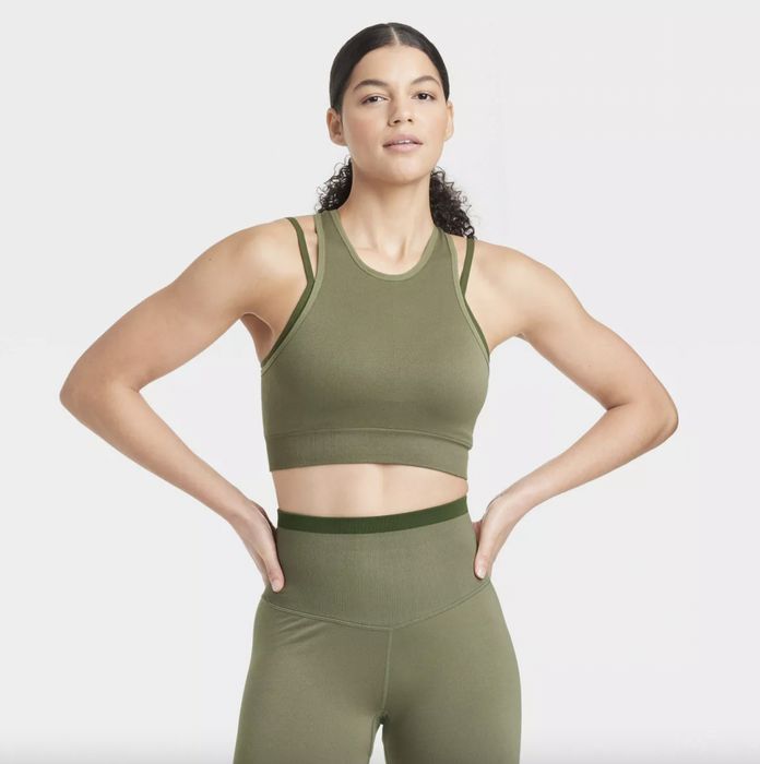 A woman in olive green athletic attire with her hands placed confidently on her hips.