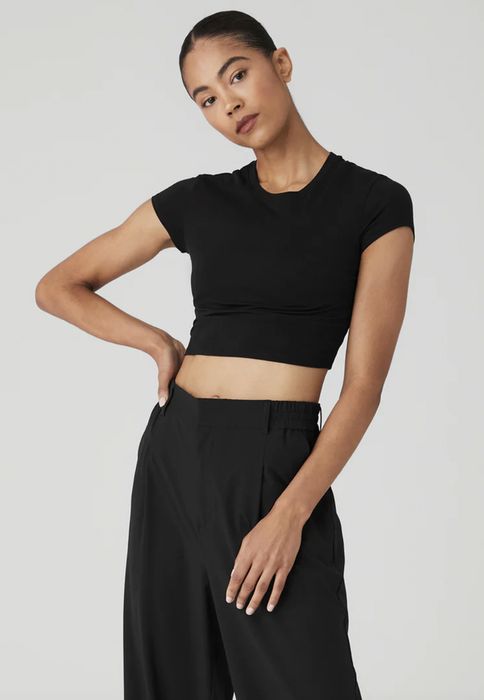 A person posing in a black crop top and high-waisted trousers, hand resting on their hip.