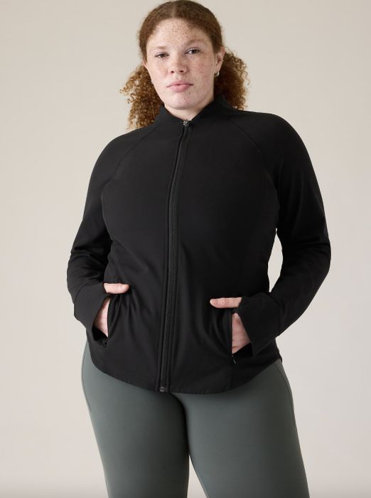 A woman in a black jacket and grey leggings, with hands placed on her hips.
